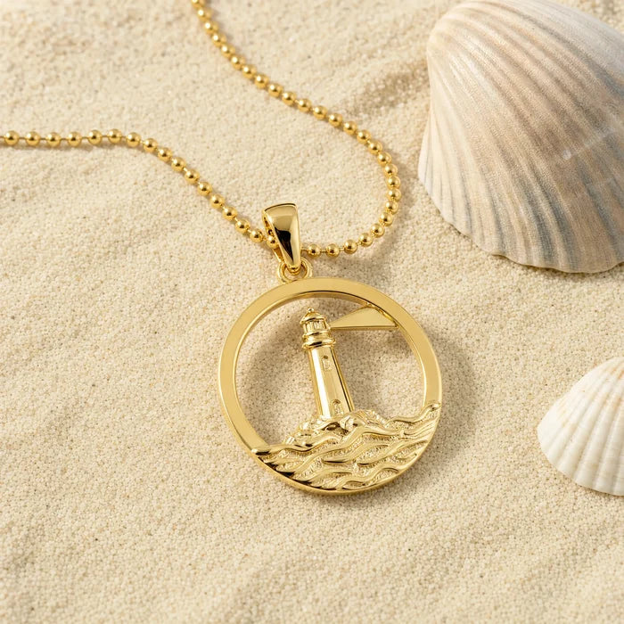 Anhänger Leuchtturm Rund / Küste vergoldet, goldene Kette auf Sand mit Muscheln.